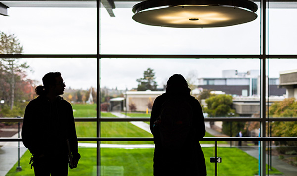 Silhouette of students standing by window at South Seattle College green grass and grey sky in background